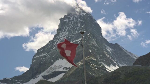 Swiss flag waving in the wind with the iconic matterhorn mountain peak in the background on a sunny day