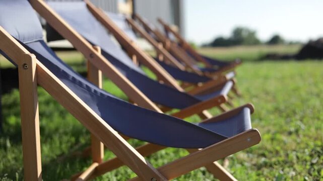 Empty luxury lounge chairs on the grass under the sun. Sun Loungers on green grass in vibrant garden, handheld view.