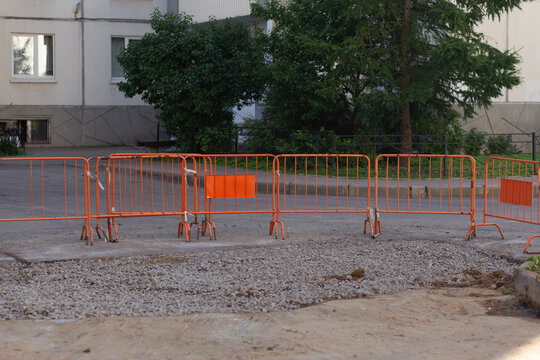 Orange safety barriers on a city roadwork site near buildings, urban infrastructure repair, public safety, construction zone, municipal maintenance.