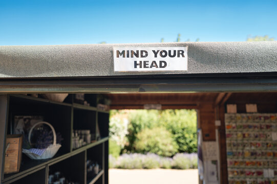 Shallow focus of a gerbil Mind Your Head sign attached to a felt roof of a small garden accessory shop seen in the grounds of a garden nursery in the UK.