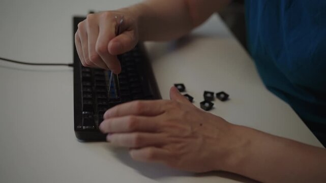 Close-up of person using keycap puller to remove and disassemble keys from mechanical keyboard for cleaning, maintenance, customization. Concept of technical repair process. Shooting in slow motion