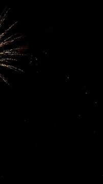 Upward view of bright fireworks bursting across dark night sky, with golden spark trails, red glowing tips, drifting smoke, and layered diagonal light lines forming dramatic