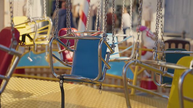 Empty colorful seats of a swing ride spinning slowly at a vintage funfair with a warm, nostalgic atmosphere, evoking memories of childhood joy and summer holidays at an amusement park