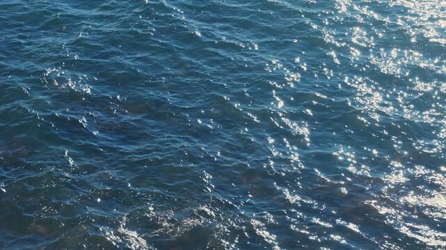 Tranquil deep blue sea water surface rippling with the sunlight reflecting and creating a glistening, sparkling texture, a perfect relaxing and meditative nature background in slow motion