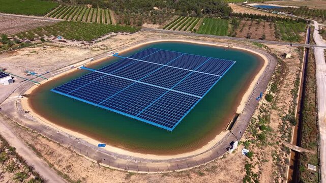 Top-down view of a floating photovoltaic solar array covering an irrigation reservoir amid orchards, combining renewable energy with water conservation and reducing evaporation on agricultural land