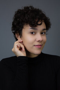 Lovely young woman touching her earlobe. Studio headshot with copy space, ideal for beauty portrait, earrings add, and hearing issues. Neutral colors.