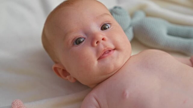 Baby newborn bare chest gazing upward with drool on lip and knitted toy nearby in studio; calm curiosity.