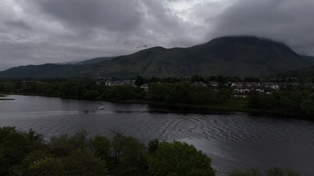 Aerial drone push forward shot of Ben Nevis in Scotland. Shot from the town Fort William over a lake with surrounding trees at night.