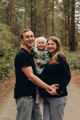 Fototapeta premium A warm family walk along a forest path. Parents are spending time with their child amidst tall trees and nature.