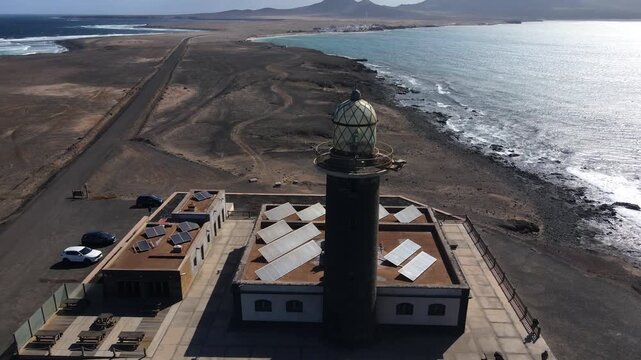 Aerial shot slowly orbiting the Punta de Jandia lighthouse. Sustainable solar panels power the structure on the remote volcanic coastline