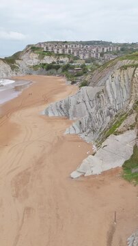 Aerial pull-back over layered flysch cliffs and beach cove, Basque coast, Spain