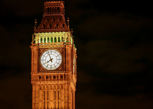 London Clock Tower At Night. Illuminated view of Big Ben featuring the glowing dial against a dark sky.