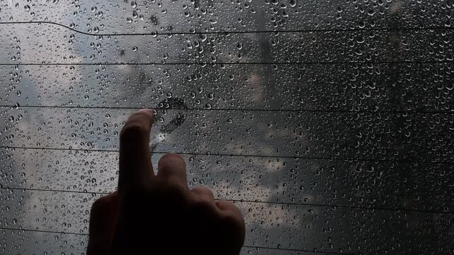 Person draws a heart shape on a foggy, rain-covered car window. Creative, moody, and contemplative moment symbolizing love and connection on a rainy journey. 4K
