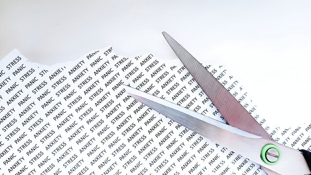 Cutting paper sheet with printed text stress, anxiety and panic using scissors. Mental health therapy and recovery concept.