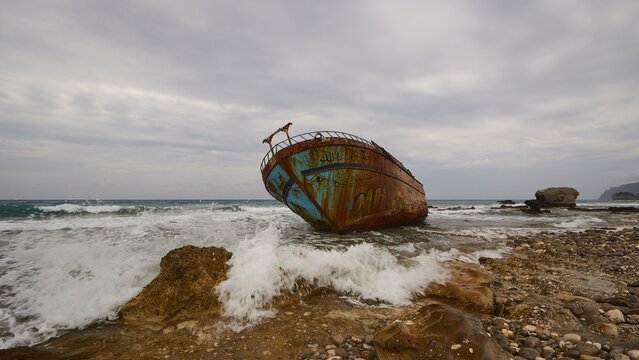 Agios Gordios, bad weather, cloudy sky, shipwreck, graffiti painting, surf, wide angle close-up, in the foreground rocky coastline and onrushing sea, wreck from diagonal below, rusty, colourfully painted, Corfu Island, Ionian Islands, Greece