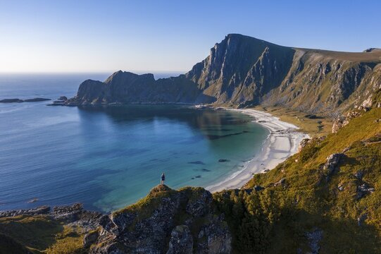 Hiker standing at the precipice, cliffs, beach and sea, in the back peak of the mountain M&aring;tinden, near Stave, Nordland, Norway