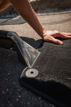 Hand pressing roofing membrane onto flat roof during installation in bright daylight, showing careful smoothing work, black material texture, seam detail, and strong outdoor shadows