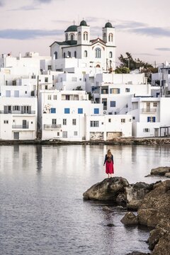 Young woman standing on a rock, town view with church, Naoussa harbour town, Paros Island, Cyclades, Greece