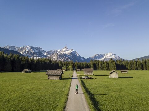 Female hiker on a trail, hay barns in a meadow, Ehrwalder Sonnenspitz and mountains, near Ehrwald, Mieminger Kette, Tyrol, Austria