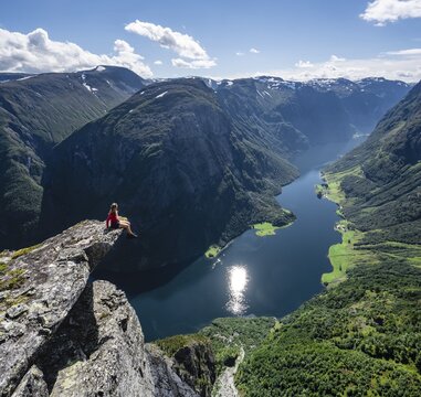 Hiker sitting on rock, view from the top of Breiskrednosi, mountains and fjord, N&aelig;r&oslash;yfjord, Aurland, Norway
