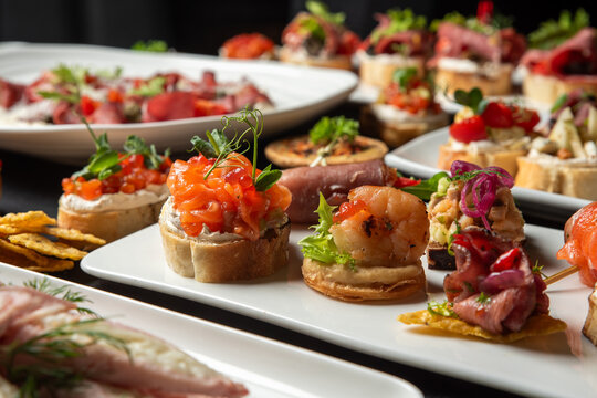 A selection of gourmet catering appetizers and canapes with salmon, shrimp, prosciutto, and caviar on white plates, perfect for a party buffet or holiday celebration.