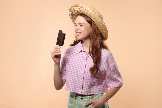 Happy teenage girl with delicious chocolate-glazed ice cream on beige background