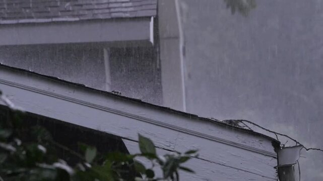 Heavy rain falling onto roof of a house. Storm winds blow the pouring rain sideways into the shingles of the roof. Sticks are blown into the gutters.