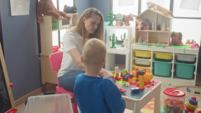 Woman helping a boy stack colorful toy blocks on a play table with hands in building; care learning together.