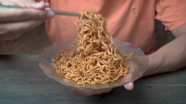 Man eating instant fried noodles with chopsticks at home, close-up comfort food concept, hungry expression, casual lifestyle.