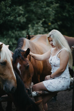 A blonde woman walks with horses in the forest