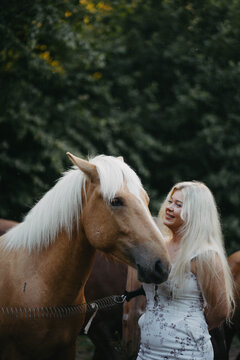 Blonde woman with horses in the garden in summer