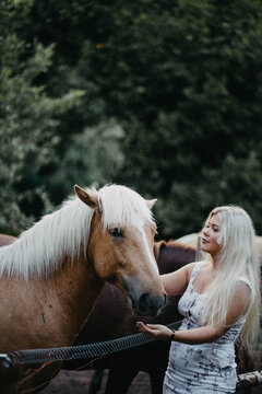 A blonde woman is walking with a horse on a ranch