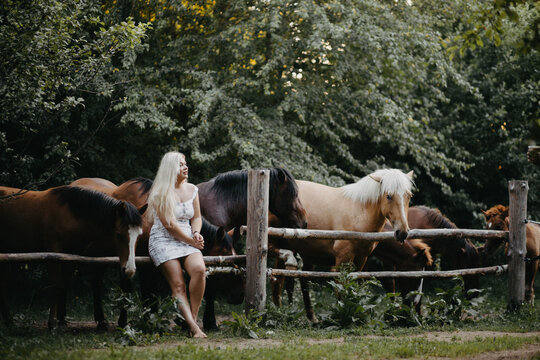 A blonde woman is walking with a horse on a ranch