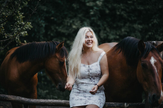 A blonde woman is walking with a horse on a ranch