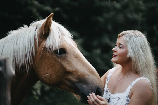 A blonde woman walks with horses in the garden in summer