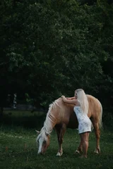 A blonde woman walks with horses in the garden in summer © velimir