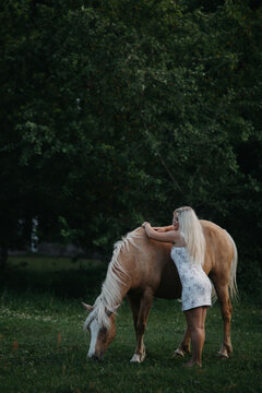 A blonde woman walks with horses in the garden in summer