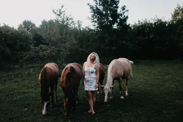 A blonde woman walks with horses in the garden in summer © velimir