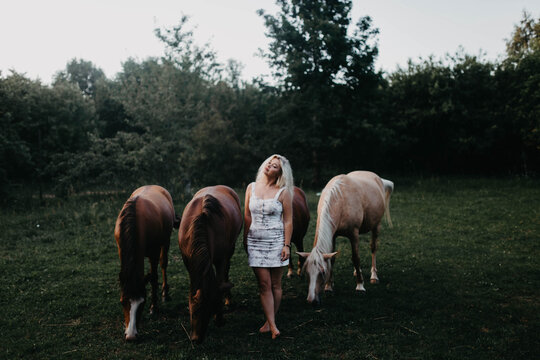 A blonde woman walks with horses in the garden in summer