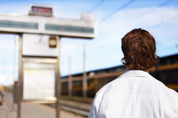 male passenger stands on a train station platform, looking at the departure board. The traveler is waiting for his connection to begin his journey. © Kyrylo