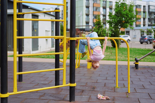 Energetic child hangs upside down on yellow monkey bars at a vibrant urban playground