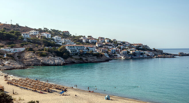Armenistis sandy Beach and village in Ikaria island, Greece. Swimmers, straw umbrellas, blue Aegean sea water, sunny summer day.