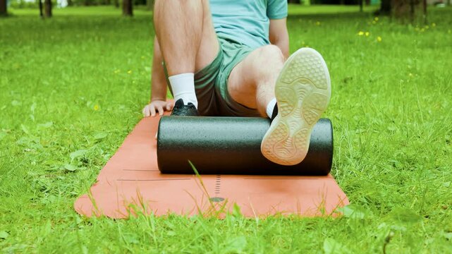 Close-up of a man doing myofascial release on his calf muscle using a foam roller outdoors. This self-massage aids post-workout recovery and relieves muscle tension. High quality 4k footage