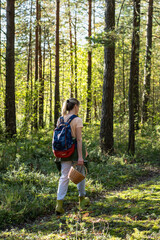 Naklejka premium Gathering edibles in wild forest, active woman forager walking through woodlands with basket searching for food, female explorer picking up mushrooms and berries in woods, organic products hunting.