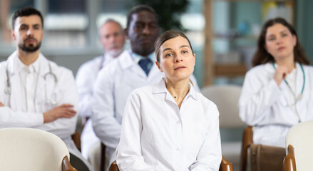 Fototapeta premium Adult female doctor listening to lecture and watching presentation with colleagues in lecture hall