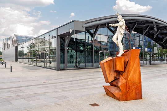 Lodz, Poland - JUNE 1, 2018; Modern Public Art Sculpture with a Rusty Geometric Base Standing in front of a Futuristic Glass Building Facade at Lodz Fabryczna in Poland