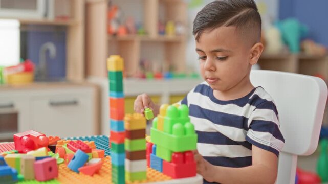 Boy stacks colorful plastic blocks with hands in a playroom, building a tall tower and concentrating on pieces; concentration curiosity.
