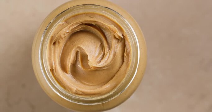 Open Jar of Peanut Butter Rotating on Warm Beige Background, Top View