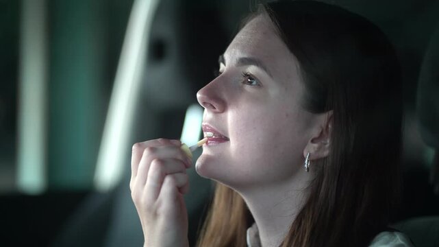 Close-up portrait of a young woman applying lip gloss in a car with soft natural light. Authentic beauty routine and self-care lifestyle footage.