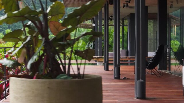 Modern luxury villa in Costa Rica features elegant wooden deck terrace with comfortable seating area surrounded by tropical plants and dense rainforest mountain landscape views.